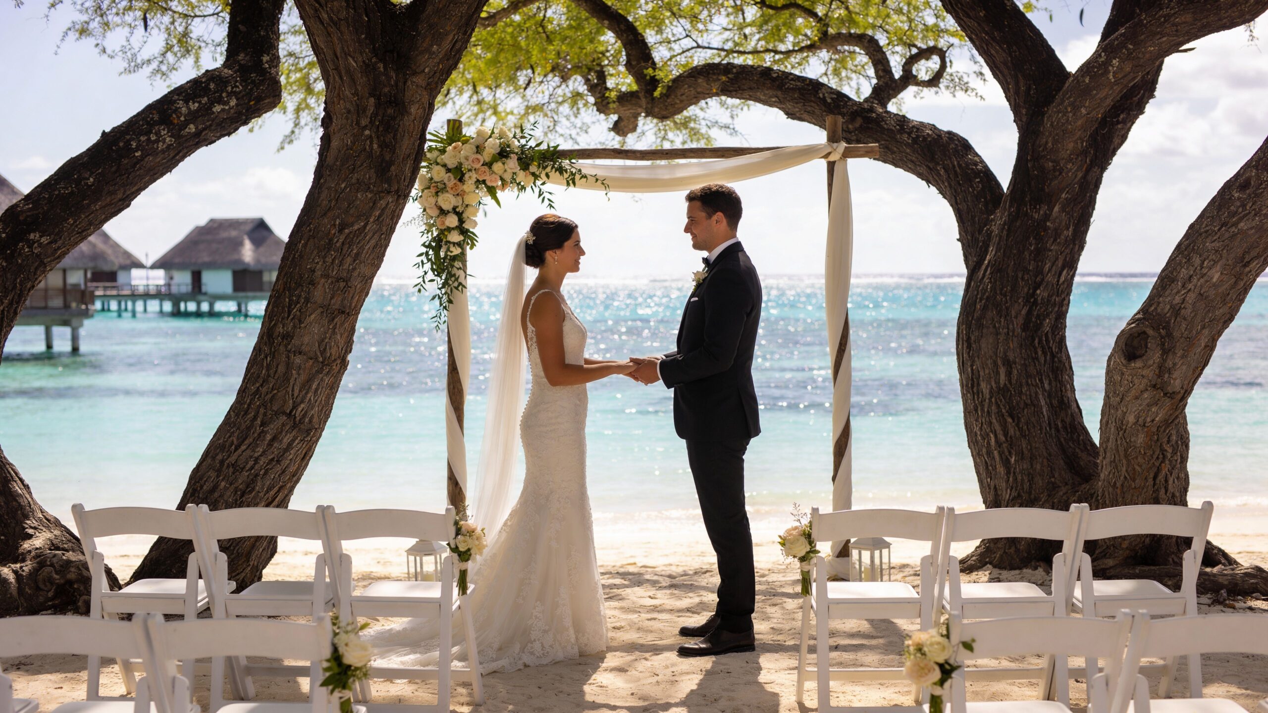 A bride and groom exchange wedding vows under a wooden arch on a beach in Mauritius.