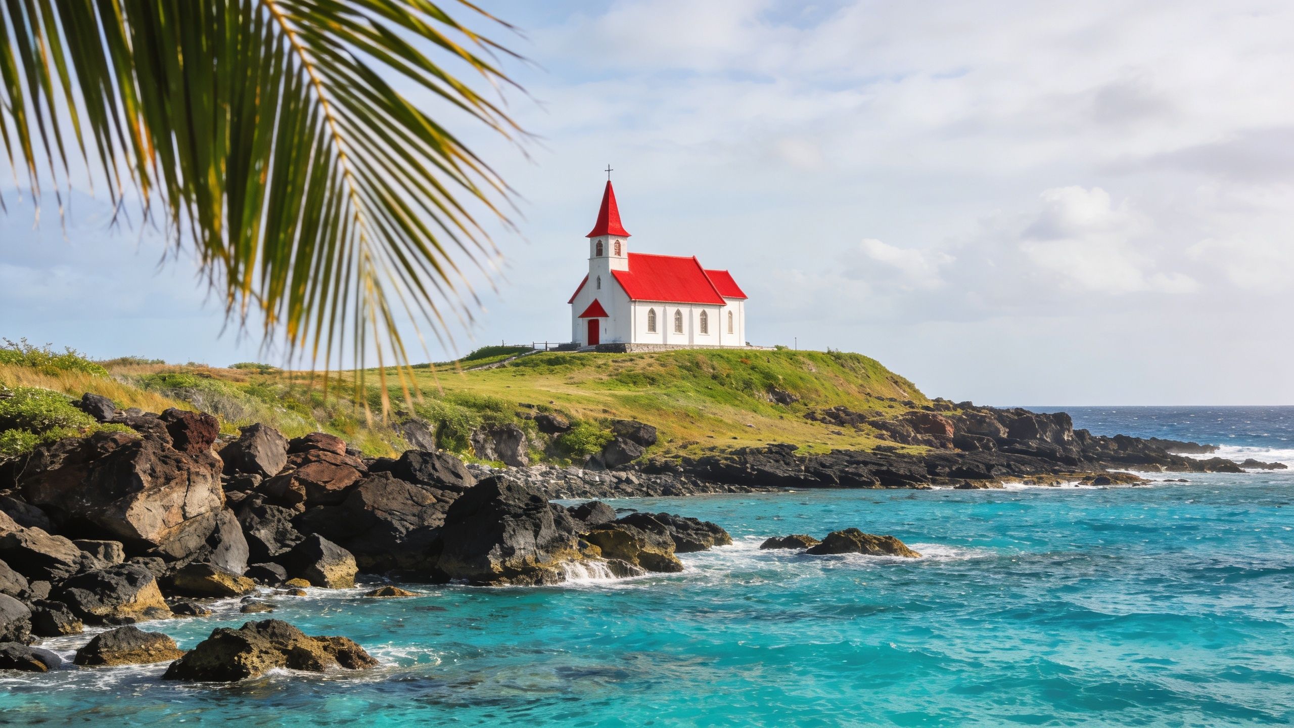 A picturesque white church with a bright red roof sits on a grassy cliff overlooking turquoise waters.