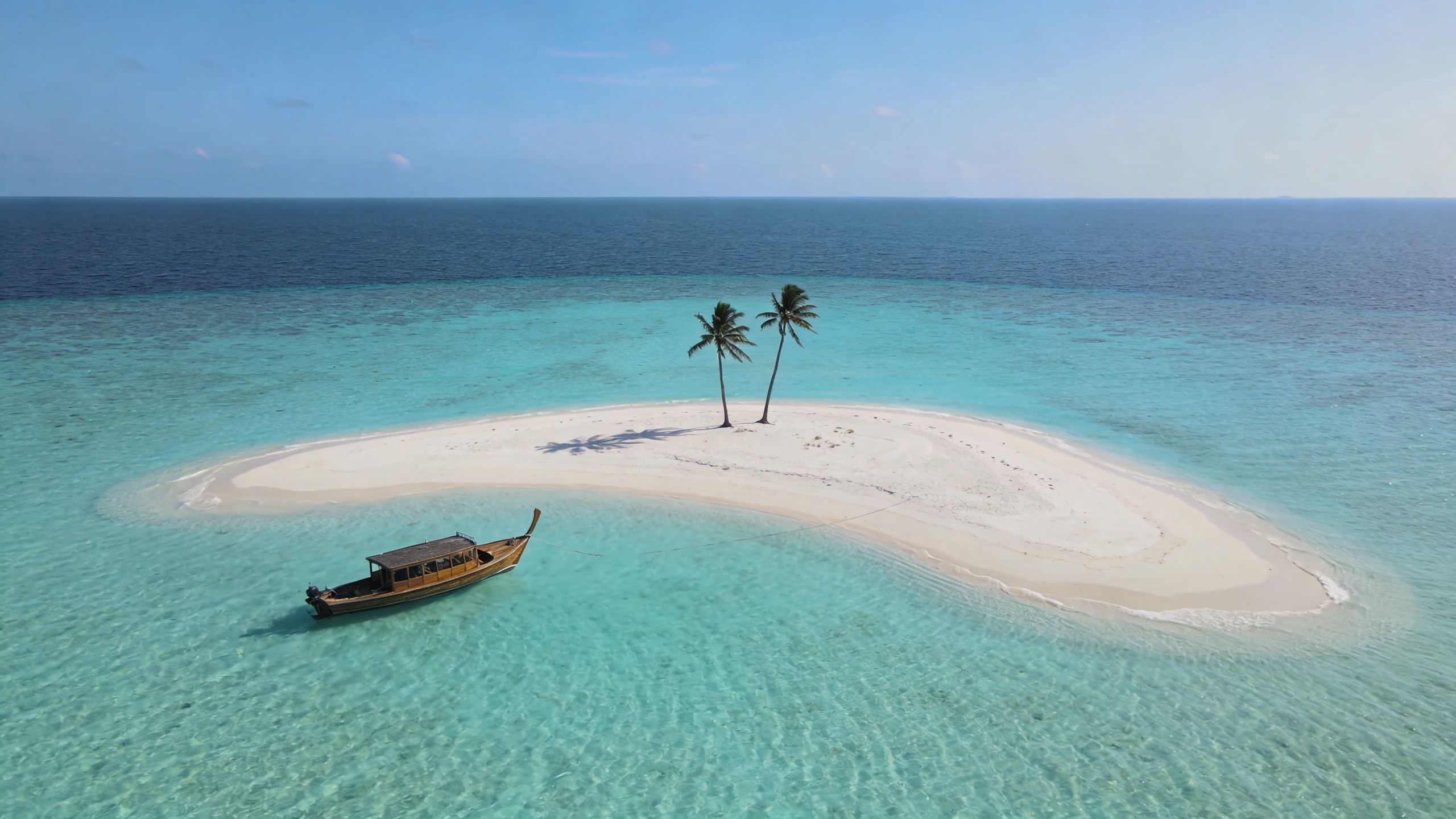 A scenic drone view of a small tropical sandbank island with two palm trees and a wooden boat.