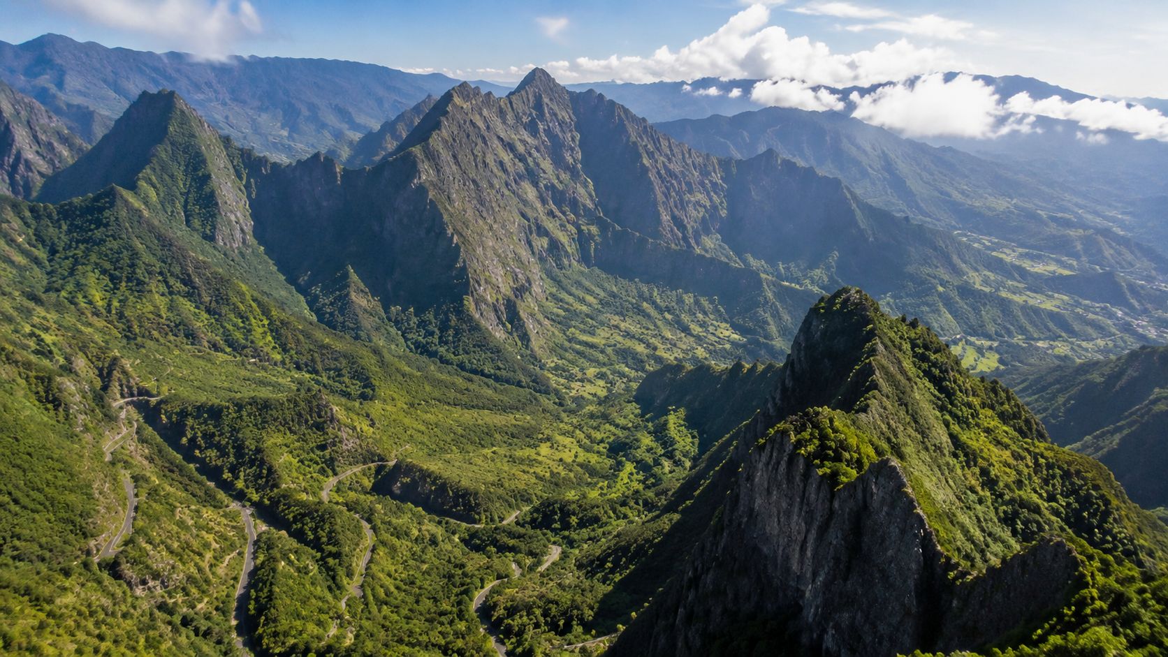 An aerial view of the lush, mountainous landscape of Reunion Island with a winding mountain road.